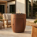 Ceramic tall cylindrical outdoor conrete fire pit with hidden propane enclosure door with flames on a patio with outdoor furniture