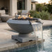 Concrete grey round fire pit with flames and water feature next to a pool
