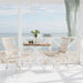 White rattan outdoor dining armchair beside a round teak café table with a white pedestal base.