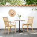 Natural rattan outdoor dining armchair beside a round teak café table on a sunny patio.