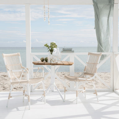 White rattan outdoor dining side chair beside a round teak café table with a white pedestal base.
