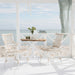 White rattan outdoor dining side chair beside a round teak café table with a white pedestal base.