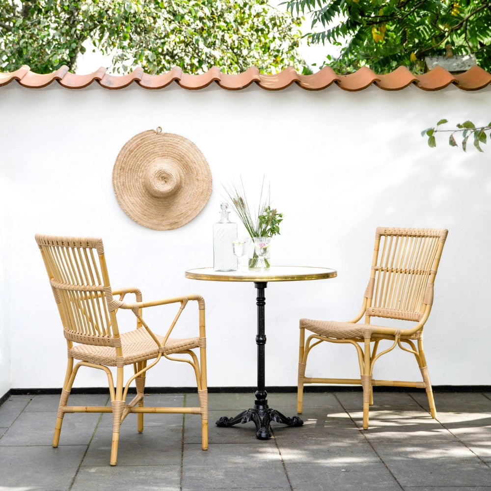 Natural rattan outdoor dining side chair beside a round café table on a sunny patio.