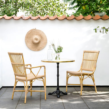 Natural rattan outdoor dining side chair beside a round café table on a sunny patio.