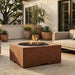 Outdoor patio with a square concrete outdoor fire pit table, potted plants, and a sofa.