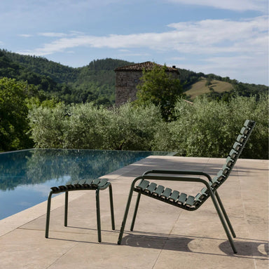 Dark green outdoor lounge chair paired with matching footrest, placed beside the pool surrounded with greenery
