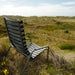 Modern black outdoor lounge chair with slatted design on a grassy dune landscape