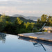 Dark green patio rocking chair beside the pool, surrounded by greenery, overlooking distant hills