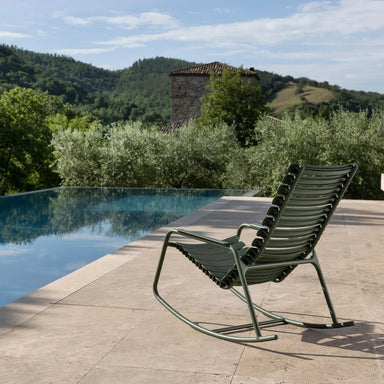 Dark green modern outdoor rocking chair beside a pool, surrounded by greenery
