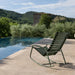 Dark green modern outdoor rocking chair beside a pool, surrounded by greenery