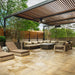 Outdoor patio with pergola, cushioned sectional sofa, dark gray rectangular fire pit, and and greenery surrounding the space.