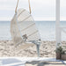 White rattan outdoor hanging swing chair featuring a white cushion and woven frame.