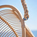 Close-up of the natural rattan outdoor hanging swing chair with a braided suspension rope and woven frame.