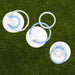 Three white circular plastic discs with blue and clear rings, each with a small white cross-shaped piece, arranged on green grass.