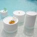 Four round white tables featuring an assortment of fruits and beverages on their surfaces.