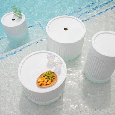 Four white round tables displaying a selection of fruit and drinks for guests.