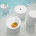 Four white round tables displaying a selection of fruit and drinks for guests.