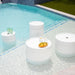 A serene pool scene featuring white round tables and a colorful bowl of fresh fruit nearby.