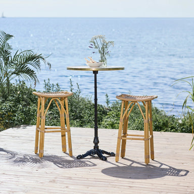 Natural rattan outdoor bar stool beside a round teak bar table with a black pedestal base.