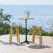Natural rattan outdoor bar stool beside a round teak bar table with a black pedestal base.
