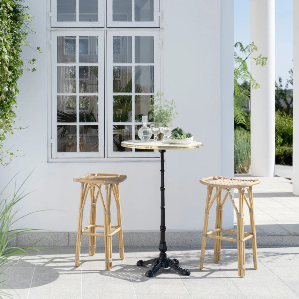 Natural rattan outdoor bar stool beside a round teak bar table with a black pedestal base.