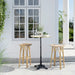 Natural rattan outdoor bar stool beside a round teak bar table with a black pedestal base.