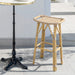 Natural rattan outdoor bar stool beside a round teak bar table with a black pedestal base.