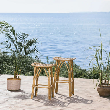 Natural rattan outdoor counter stools on a wooden deck with an ocean view.
