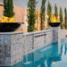 A two black round concrete fire and water bowls placed on a tiled wall with multiple waterspouts beside the pool 