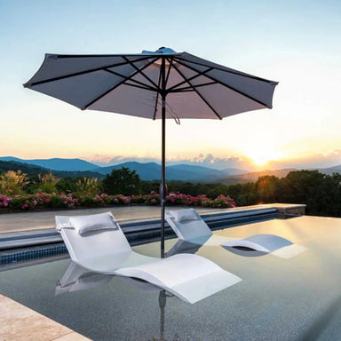 Two modern in-pool chaise with headrest pillows partially submerged on a pool sunshelf under an outdoor umbrella, with sunset and mountain views.