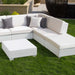 White outdoor sectional sofa set with matching ottoman on a green lawn, styled with white and gray throw pillows in a backyard setting.