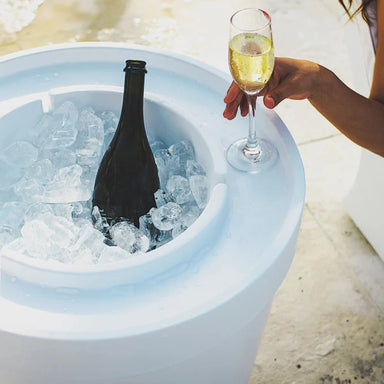 Modern white in-pool round ice basin filled with ice, a wine bottle, and a woman’s hand holding a glass of wine.