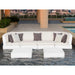 A modern outdoor sectional sofa set in white with gray and white throw pillows, positioned in front of a pool on a rooftop terrace with a city skyline in the background.
