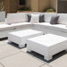 White outdoor in-pool sectional sofa with gray and white throw pillows, paired with two matching white cube-shaped in-pool coffee tables on a light stone patio.