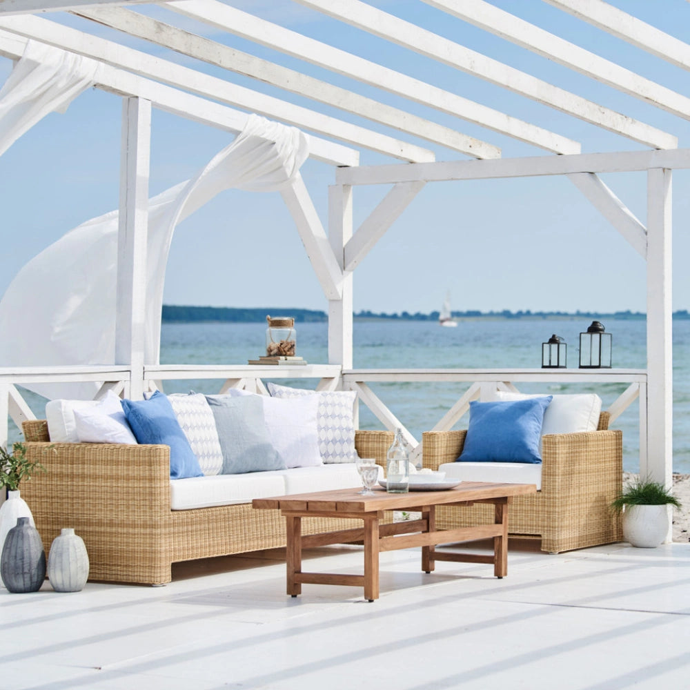 Natural rattan outdoor 3-seater sofa with white and blue cushions beside a teak coffee table.