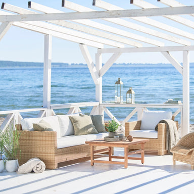 Natural rattan outdoor 3-seater sofa with white cushions beside a matching lounge chair.