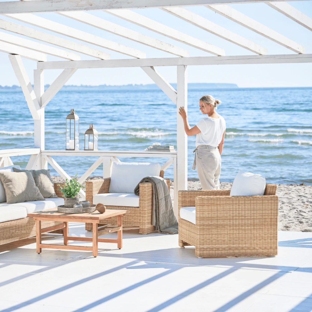 Natural rattan outdoor lounge chair with white cushions beside a woman overlooking the ocean.