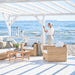 Natural rattan outdoor lounge chair with white cushions beside a woman overlooking the ocean.