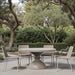 Outdoor patio with beige round concrete outdoor dining table and four beige wicker chairs surrounded with greenery