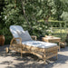 Natural rattan outdoor square side table beside a matching chaise lounge in a garden setting.