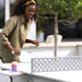 A woman wearing a khaki button-up shirt and a yellow headband is playing ping pong on an outdoor table tennis table.