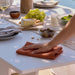 Person setting a table with a white tablecloth, wine glasses, and food items.