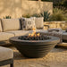 Outdoor patio scene with a round concrete fire pit table and comfortable seating area.