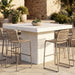 Outdoor patio with square white concrete bar table, beige wicker high chairs, surrounded by greenery