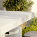 Close-view of a white concrete outdoor dining table with speckled texture, surrounded by greenery