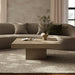 Modern living room with square beige concrete coffee table in front of a  curved sofa over a textured rug