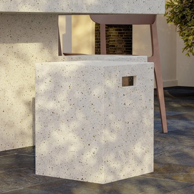 White speckled concrete outdoor stool beside a beige chair on a dark tiled floor with some greenery visible
