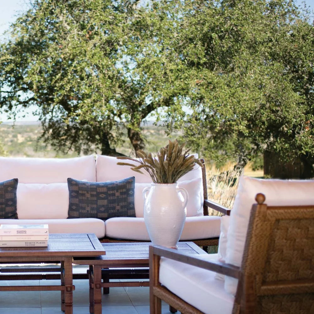 Outdoor patio set with white cushions, wooden armchair, and coffee table under a tree.