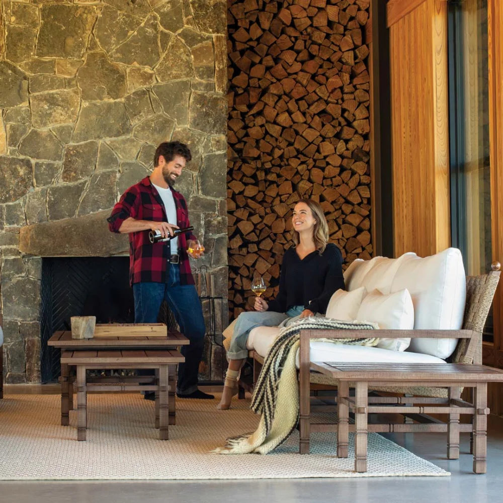 Man and woman in a cozy living room with stone fireplace and woodpile.