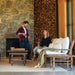 Man and woman in a cozy living room with stone fireplace and woodpile.
